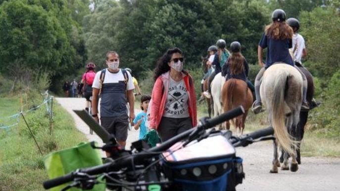 Pla obert on es veu un grup de persones passejant i altres a sobre d'un cavall passant per un camí que discorre a l'entorn del riu Segre a Isòvol i part d'unes bicicletes desenfocades en primer terme.